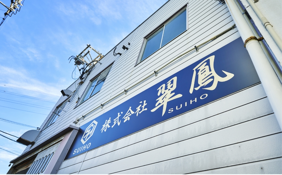 株式会社翠鳳の社屋の外観です。白色の壁に社名の入った青色の看板が掲げられています。